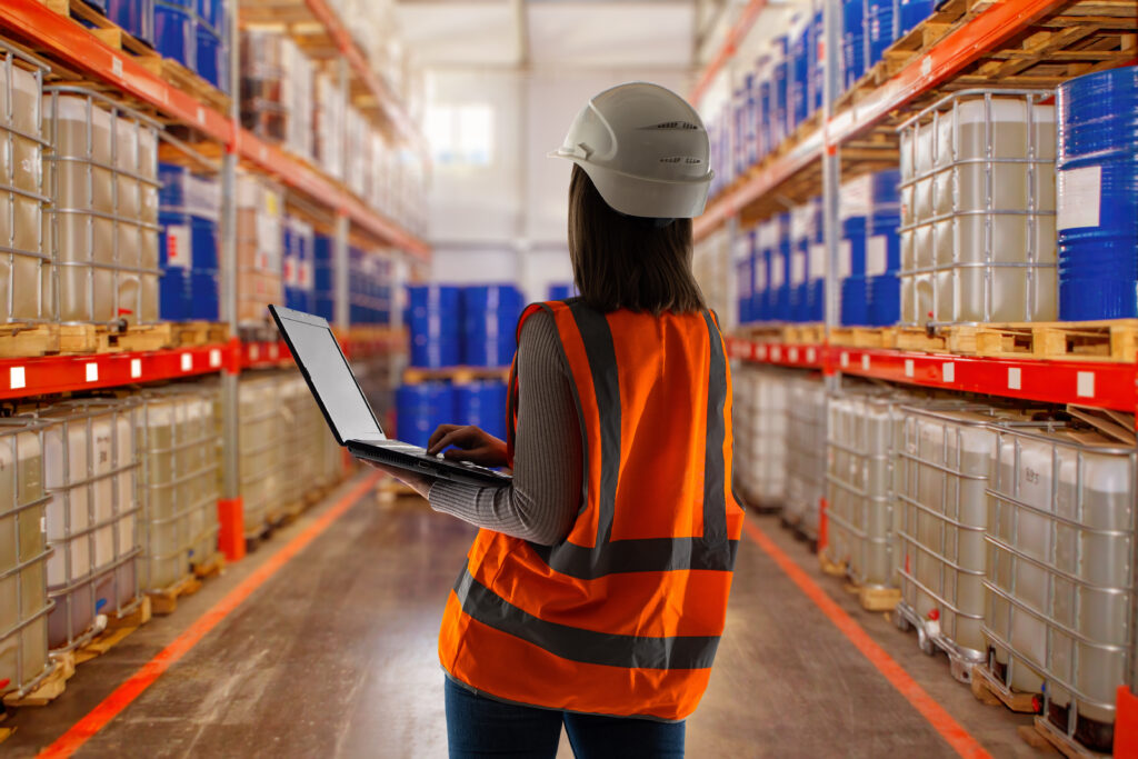 Warehouse worker woman. Storage of fuels and lubricants. Shelving with tanks for storage of petroleum products. Woman storekeeper with laptop. Oil warehouse supervisor back to camera